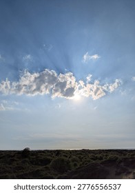 Sun Rays Breaking Through Clouds Over Coastal Dunes And Sea Horizon