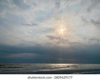 Sun rays breaking through clouds over ocean, clouds air scenery sun light blue sky. Beautiful landscape with golden sun lights penetrated through dark clouds. White water hitting the beach with small waves. Idea for natural, oceanic, and landscape themes.