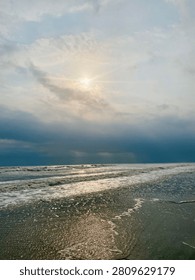 Sun rays breaking through clouds over ocean, clouds air scenery sun light blue sky. Beautiful landscape with golden sun lights penetrated through dark clouds. White water hitting the beach with small waves. Idea for natural, oceanic, and landscape themes.