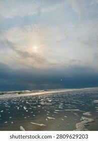 Sun rays breaking through clouds over ocean, clouds air scenery sun light blue sky. Beautiful landscape with golden sun lights penetrated through dark clouds. White water hitting the beach with small waves. Idea for natural, oceanic, and landscape themes.