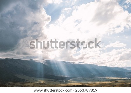 Sun rays breaking through clouds, illuminating a lush valley and mountains