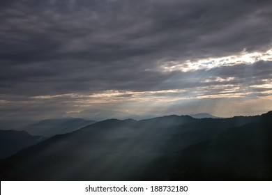 Sun rays breaking through dark clouds over mountains. Darjeeling, Himalayas, India