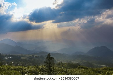 Sun rays breaking through dramatic clouds over a lush tropical mountain landscape, creating a peaceful and ethereal atmosphere. Perfect for themes of nature, travel, and tranquility.