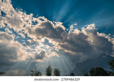 Sun Rays Breaking Through Dramatic Clouds Over Mountain Landscape. Spectacular sun rays streaming through dramatic clouds above a mountain landscape. The sunlight creates crepuscular rays across the sky, producing a stunning natural scene with atmospheric light, cloud formations, and scenic wilderness.