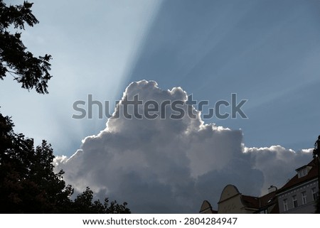 Sun rays bursting from behind dramatic storm clouds above the city skyline. Spectacular crepuscular rays illuminate sky, creating powerful atmospheric weather scene with natural light and contrast.