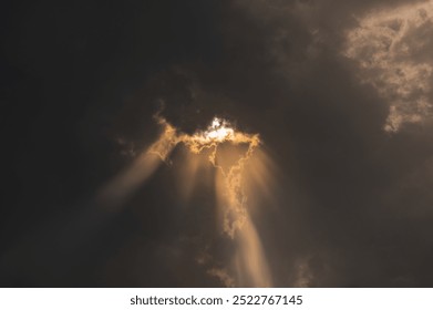 Sun rays coming out from the dense black rain clouds which makes beam of light rays and highlights the edge of clouds.