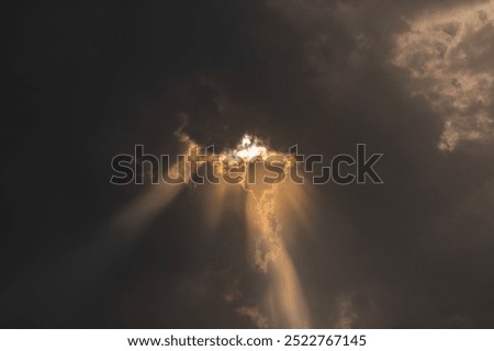 Sun rays coming out from the dense black rain clouds which makes beam of light rays and highlights the edge of clouds.