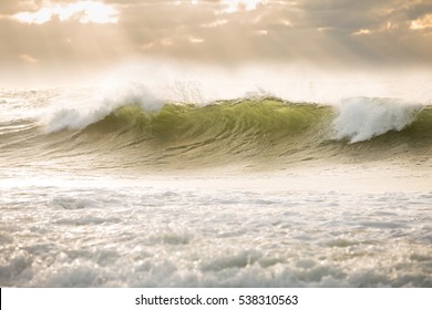 Sun rays cut through an overcast sky while a wave breaks in the Atlantic Ocean.
