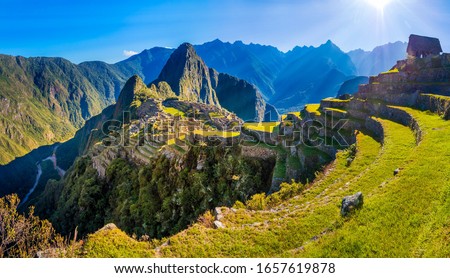 Sun rays over Inca city of Machu Picchu and the terraces around it with a nice blue sky, just after sunrise. Near Cusco, Peru. Unesco World Heritage site, one of the new wonders of the world. 