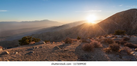 Sun Rays Over Mountain Range In Desert. This Is A Panorama Image Taken Of Keys View In Joshua Tree National Park In California At Sunset. The Last Sun Rays Hover Over The Mountainous Desert Landscape.