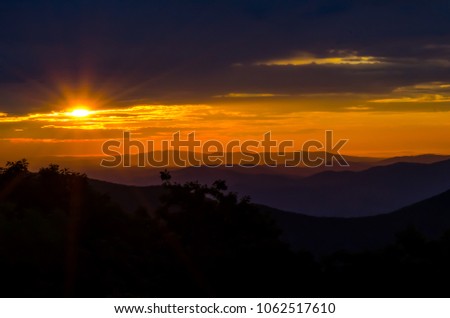 Sun rays peek through the clouds over a hazy purple mountain range