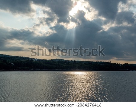 
Sun rays peeking through clouds and shining down on ocean with shore in backgound.