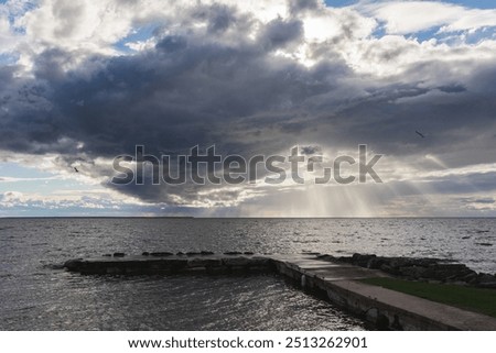 sun rays peeking through clouds over dock near water