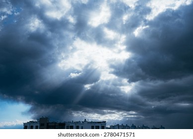 Sun rays puncturing a dark, stormy sky filled with thick clouds over a city skyline, representing hope emerging from adversity and a break in a difficult situation