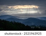 Sun rays shine through the clouds on the hilly landscape.
