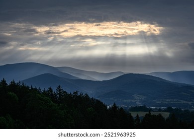 Sun rays shine through the clouds on the hilly landscape.
