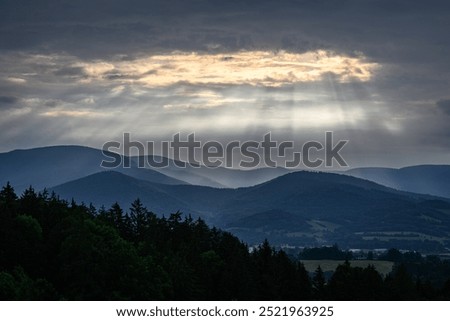 Sun rays shine through the clouds on the hilly landscape.

