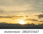 Sun rays shining behind dark dramatic clouds over mountains at sunset.