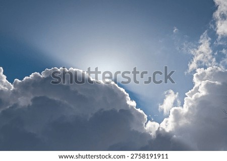 sun rays shining over het edge of a dark grey cloud on a blue sky
