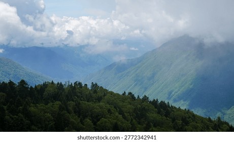 Sun rays shining through clouds over green mountain landscape in Shinhotaka, Gifu, Japan