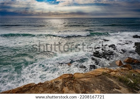 Sun rays shining through the clouds of a  threatening storm as Pacific Ocean waves break over a rocky headland foreshore at Coolum, Sunshine Coast, Queensland.