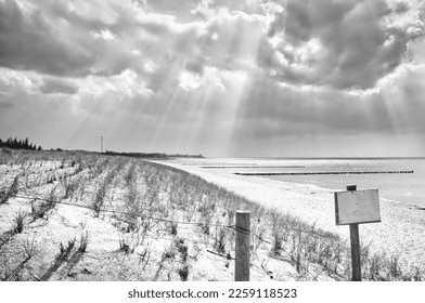 Sun rays shining through dense clouds on the beach of the Baltic Sea taken in black and white. Sign at the beach crossing. Groynes on the coast. Sandy beach in Zingst. Landscape photo from Germany - Shutterstock ID 2259118523