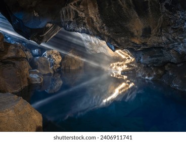 Sun rays shining through the entry of Grjótagjá cave in Iceland and reflected on hot water surface. Cave filled with crystal clear hot water is located close to Mývatn lake