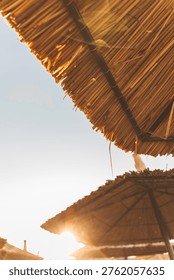 Sun rays shining through straw beach umbrellas at golden hour. Blurred, selective focus