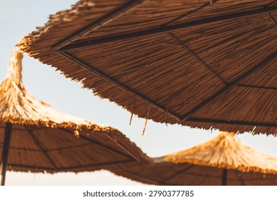 Sun rays shining through straw beach umbrellas at golden hour. Blurred, selective focus
