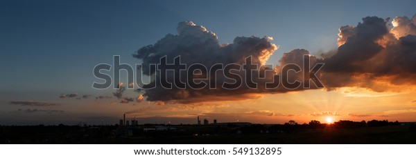 Sun\
rays sunset below cumulonimbus clouds Industrial skyline of\
constantly smoking chimneys from coal burning chemical engineering\
petroleum plant. Flames consume expelled toxic\
gas.