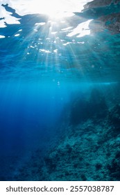 Sun rays through the clear blue waters off the coast of Orote Point, Guam, showing the descending reef wall 