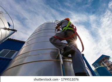 The Sun Rays Through Of Climb The Ladder Worker Height Safety Inspection Of Thickness Storage Oil And Gas Tank Industry, Concept Worker High Building Outdoors Wear Equipment Protective.