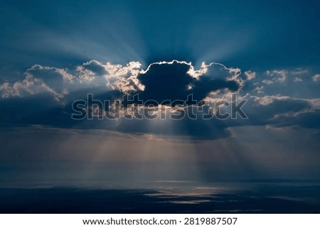Sun rays through clouds during golden hour in blue, gray, golden tones, evoking a dramatic and moody mood, a dramatic skyscape showcasing the natural scenery and outdoor environment.
