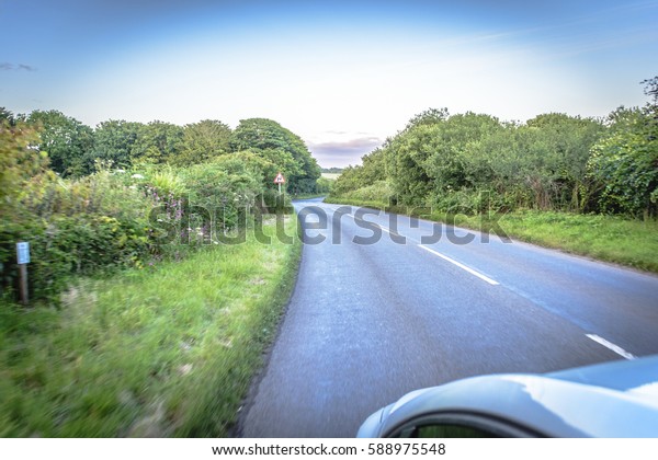 Sun rays through the forest and car on the\
street in cornwall england in\
summer