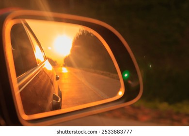 The sun is reflected in the mirror, evening road. View in the side rear view mirror of a red car driving along the highway and street