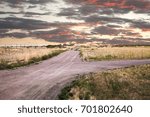 Sun reflecting off the clouds as it rises over an empty dirt road in the prairie.