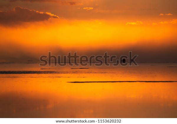 The sun and its\
reflection fallin over somer tourists during a sunset in the Salt\
Flats of Uyuni Bolivia. 