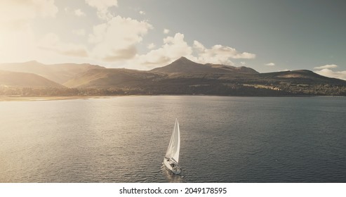 Sun reflection at ocean bay with sailboat. Aerial yacht cruise at sunlight. Summer luxury journey on sail boat at open sea. Mountain island of Arran, Scotland at cinematic seascape at soft drone shot - Shutterstock ID 2049178595