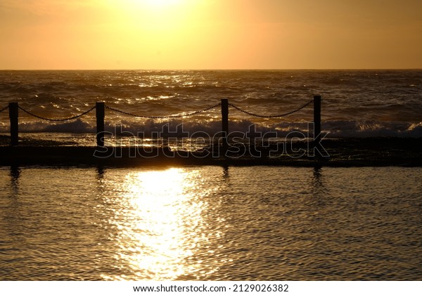 sun rise with rock pool poles divided in\
three section golden sky sea water and pool\
