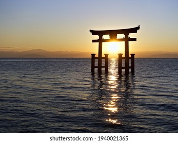 the sun rises from behind the lake between the shutters of the Shinto torii gates, standing in the water