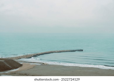 The sun rises gently over the peaceful shoreline of Constanta, illuminating the smooth waves lapping against a rocky jetty. Seagulls soar above, completing this coastal serenity - Powered by Shutterstock