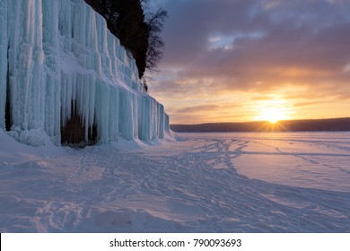 The sun rises over a frozen Lake Superior and reflects the blue hues, on Grand Island's ice curtains. Offshore from Munising Michigan