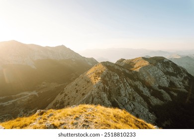 The sun rises over a mountainous terrain, casting a warm golden glow on the rocky peaks and lush valleys below, creating a serene and breathtaking view. - Powered by Shutterstock