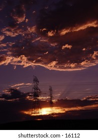 Sun rising behind clouds and powerlines.