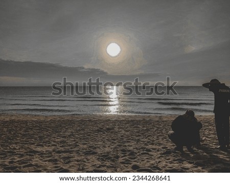 The sun is rising on the horizon of the beach.On the sandy shore, there are two figures standing on the sand.
