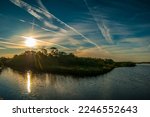 The sun is rising over a mangrove island at Betty Steflik Nature Preserve in Flagler Beach Florida. Aircraft contrails slash through the clouds. 