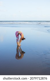 Sun Salutation practice at the beach. Slim woman standing in Uttanasana. Standing Forward Bend. Healthy lifestyle. Flexible spine. Water reflection. Yoga retreat. Copy space. Bali, Indonesia