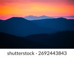 Sun sets behind the distant mountains, illuminating warm orange and purple tones over the landscape. Carpathian mountains, Ukraine. Photo wallpapers of a magical place. Discovery the beauty of earth.