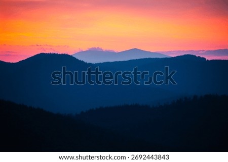 Sun sets behind the distant mountains, illuminating warm orange and purple tones over the landscape. Carpathian mountains, Ukraine. Photo wallpapers of a magical place. Discovery the beauty of earth.