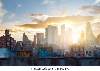 The sun sets behind the downtown skyscrapers of the Manhattan skyline with graffiti covered rooftops in New York City in 2017.